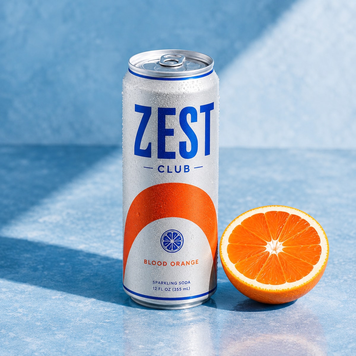A silver Zest Club blood orange soda can with cobalt branding on an icy-blue studio set