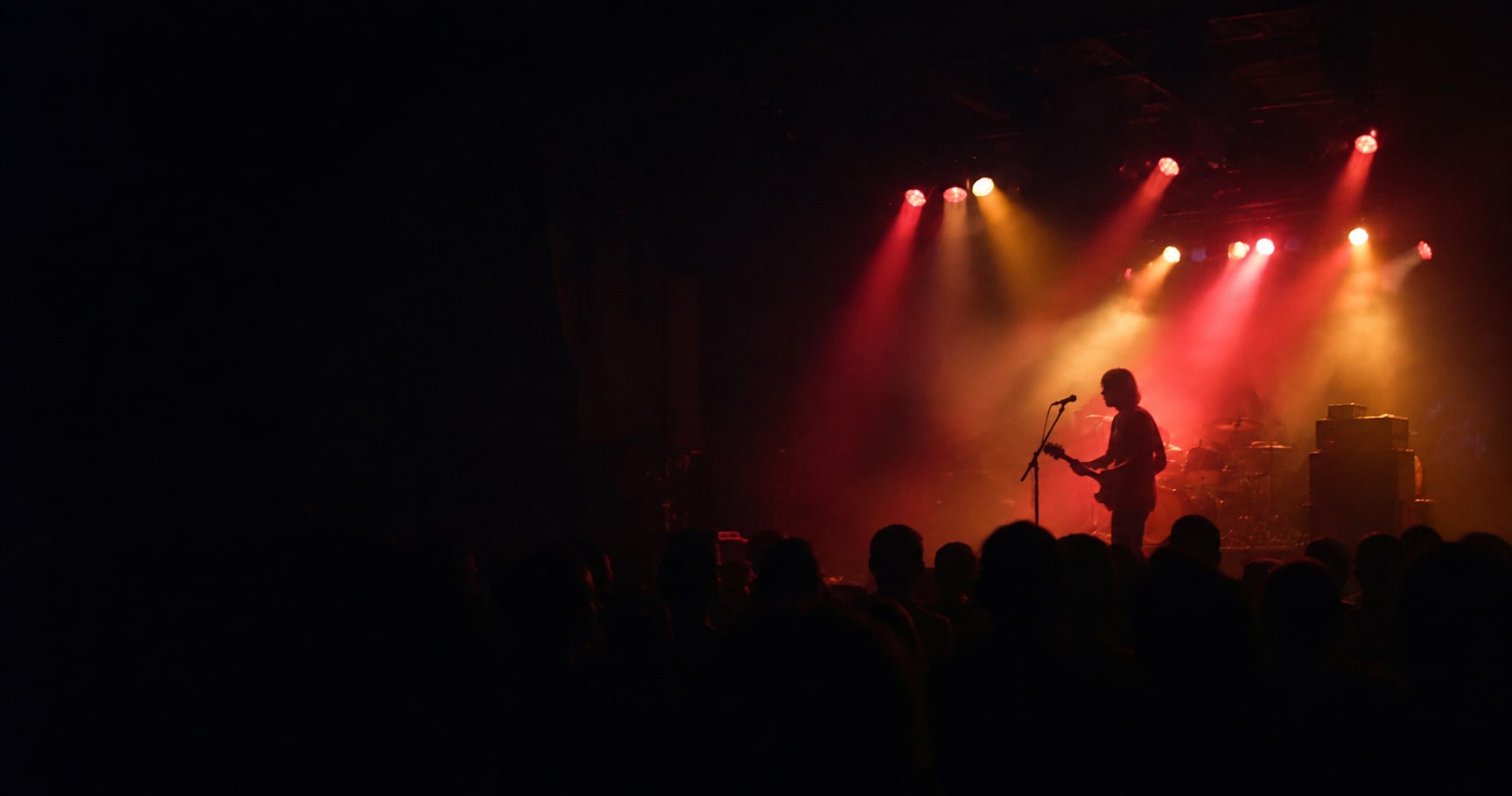 A rock guitarist on stage under red and amber lights, seen from the audience